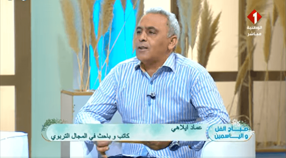 إضاءات من لقاء إعلامي: تقديم كتاب "تصوّر لمشروع الإصلاح التربوي في تونس 2025–2030" 1 أستاذ عماد إيلاهي في أستوديو القناة الوطنية الأولى، يحمل كتابه حول الإصلاح التربوي، وأمامه ميكروفون يرمز لصوت الكلمة الحرة.