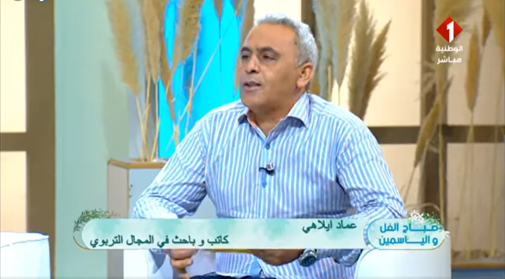 إضاءات من لقاء إعلامي: تقديم كتاب "تصوّر لمشروع الإصلاح التربوي في تونس 2025–2030" 1 أستاذ عماد إيلاهي في أستوديو القناة الوطنية الأولى، يحمل كتابه حول الإصلاح التربوي، وأمامه ميكروفون يرمز لصوت الكلمة الحرة.